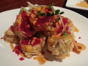 Sushi roll sliced, arranged in a pile, and covered in spicy sauce and roe.